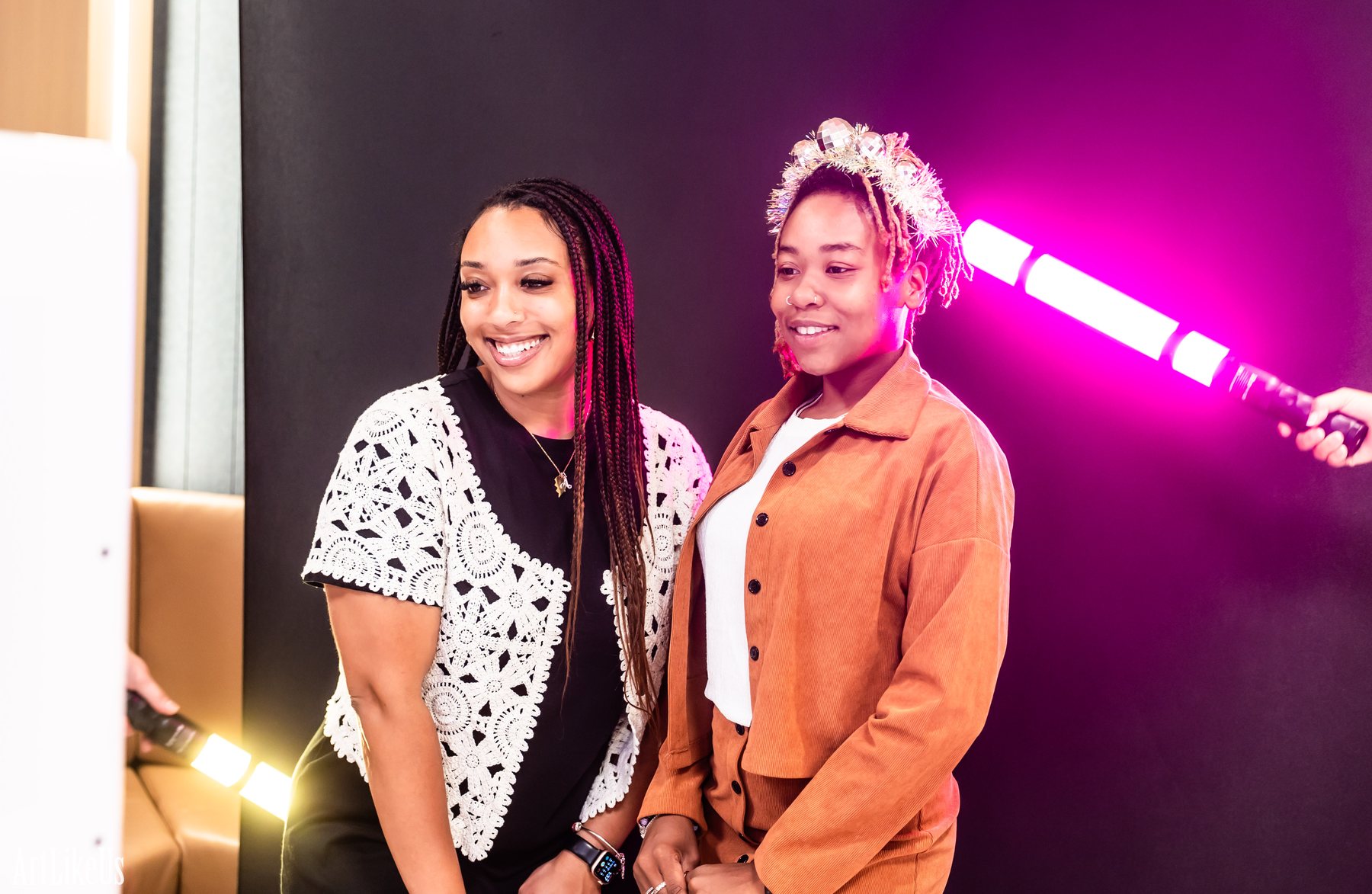 Two guests smiling together as magenta and yellow LED wand streaks cross behind them