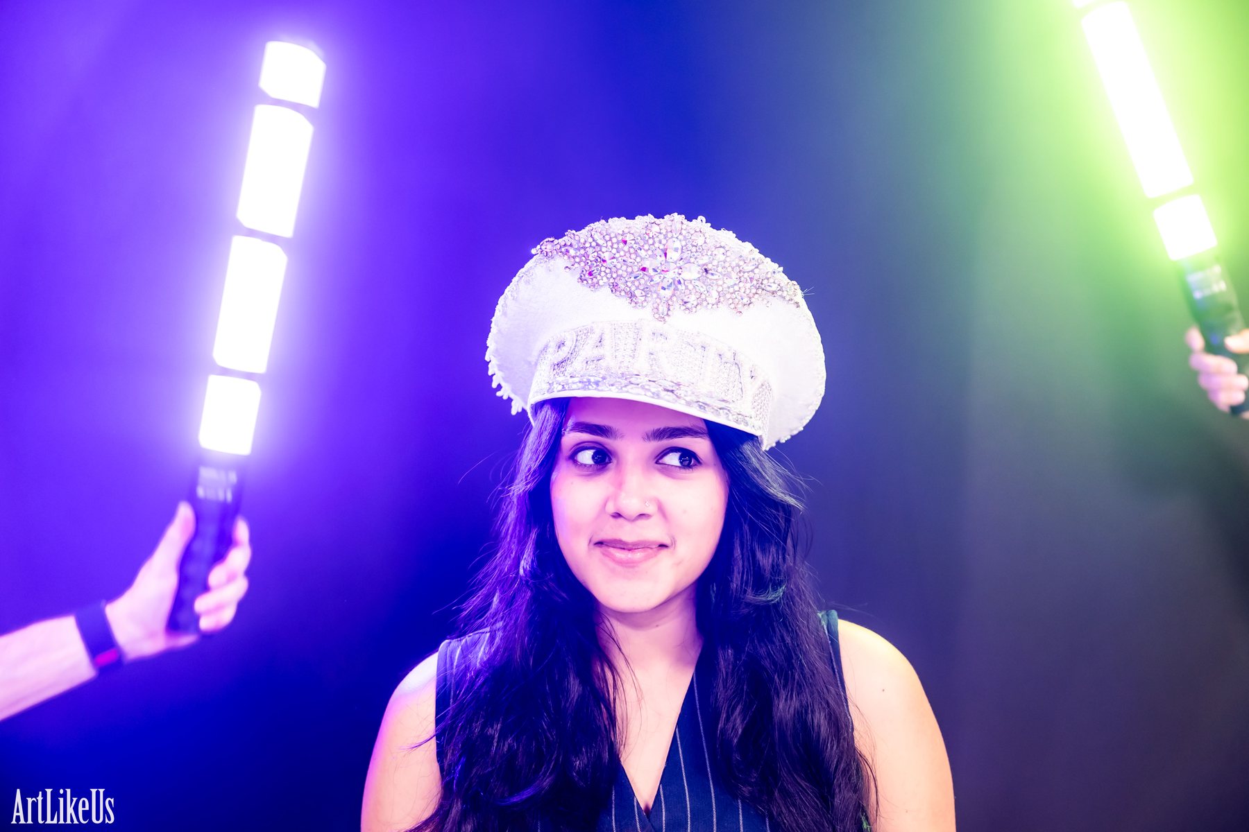 A guest in a sequined cap lit by crossed white and green LED wand streaks at the light painting booth