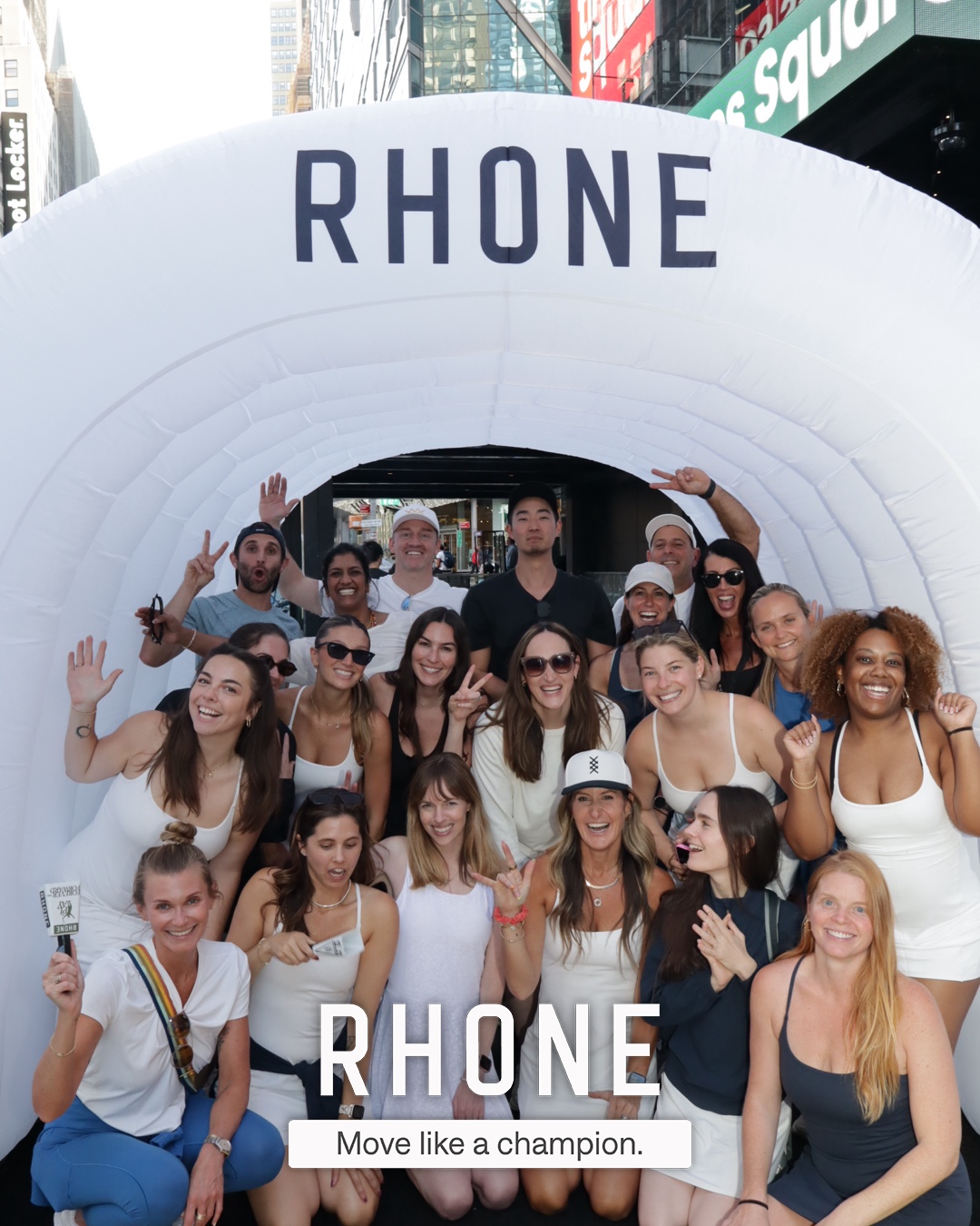 A large group of guests posing inside the branded Rhone entrance tunnel at CityPicklePalooza in Times Square, with the 'RHONE / Move like a champion.' branded overlay
