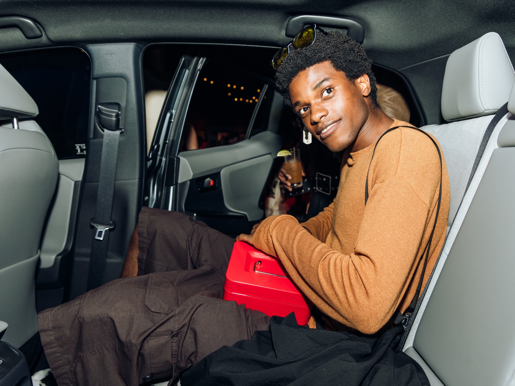 A guest in the back seat of the Toyota C-HR holding the in-car camera rig's red trigger box, mid-capture