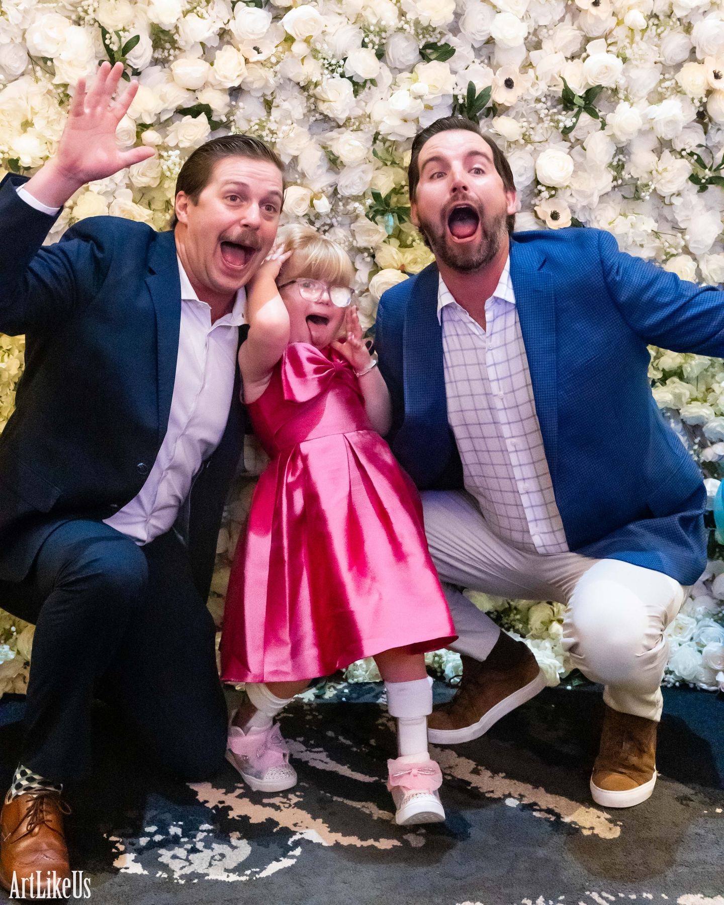 Guests laughing together at a flower-wall photo booth backdrop at a gala