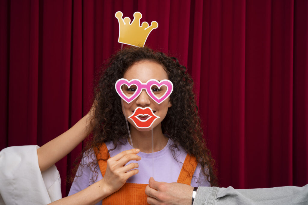 A woman posing for a photo in the photo booth with her friends holding the props for her.