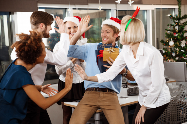 Team celebrating Christmas at corporate party with gifts and high-fives.