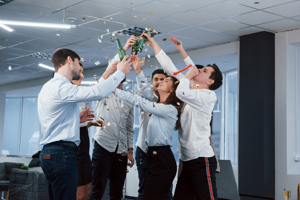 Office team celebrating with drinks, confetti, and party horns.