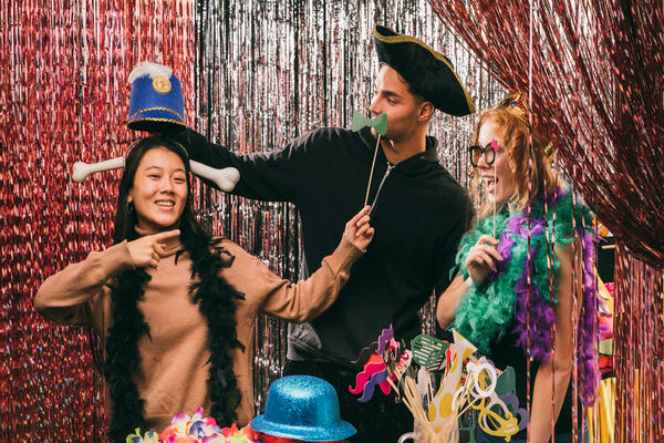 Friends posing with props in playful photobooth at party.