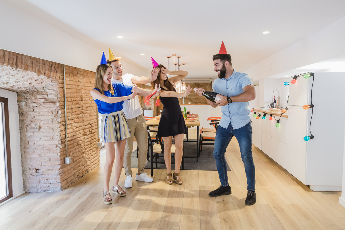 Four young adults at indoor party laughing, celebrating with champagne.