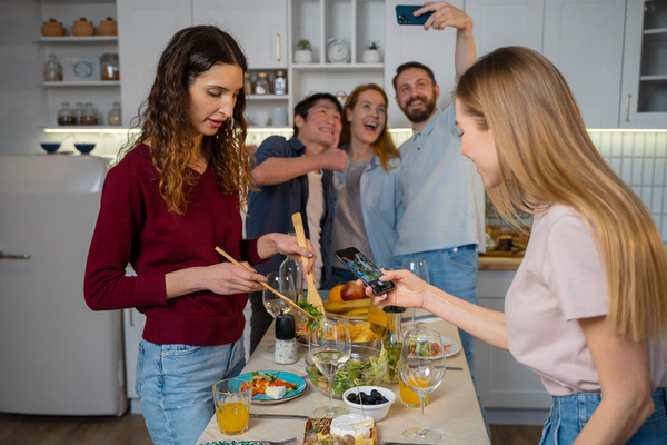 Friends preparing food and taking photos during kitchen gathering.